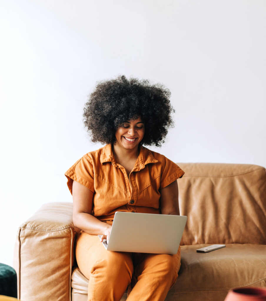 Happy woman sitting on a couch using a laptop.