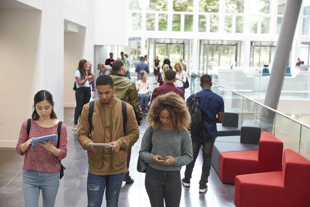 Students walk in university campus using tablets and phone